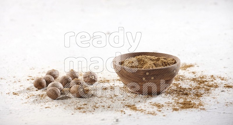 A wooden bowl full of nutmeg powder with the seeds and sprinkled powder beside it on a textured white flooring in different angles