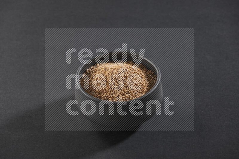 A black pottery bowl full of mustard seeds on black flooring