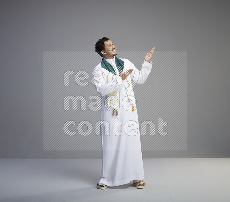 رجل سعودي يرتدي ثوب ابيض يضع شال مكتوب عليه المملكة العربية السعودية حول رقبته