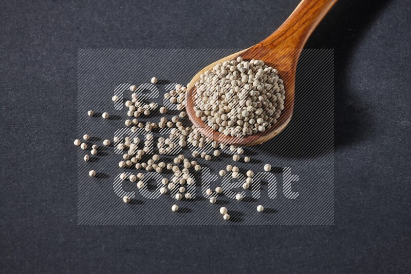 A wooden ladle full of white pepper beads on black flooring