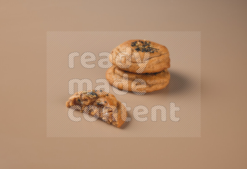 Two Hasawi cookies field of date and decorated by black seed and anise grain with another one cut in half on a brown background