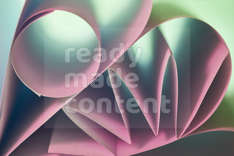 An artistic display of paper folds creating a harmonious blend of geometric shapes, highlighted by soft lighting in green and pink tones