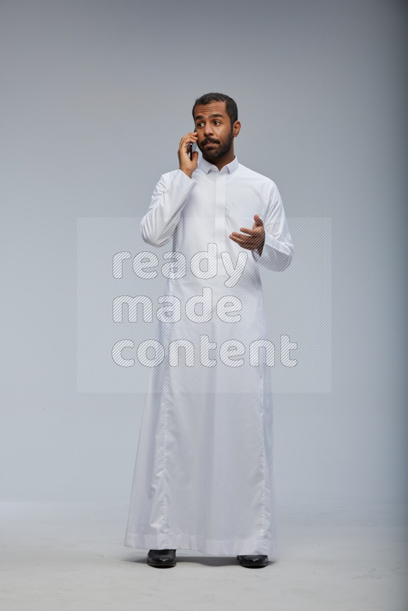 Saudi man wearing Thob standing talking on phone on Gray background
