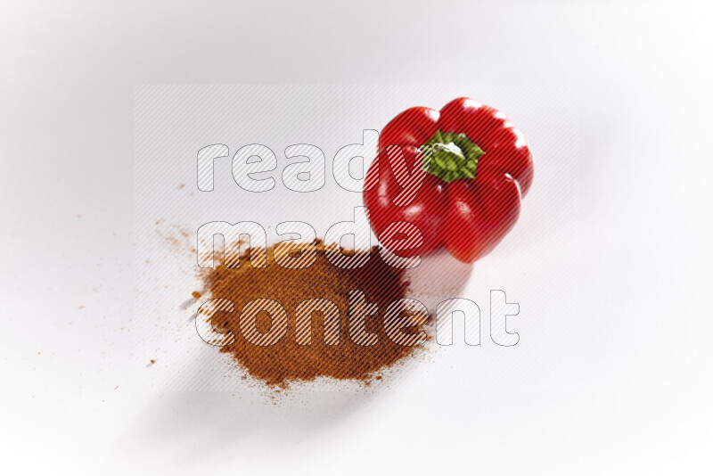 A bunch of ground paprika powder with a red bell pepper beside it on white background