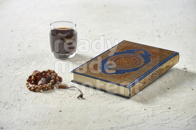 Quran with dates, prayer beads and different drinks all placed on textured white background