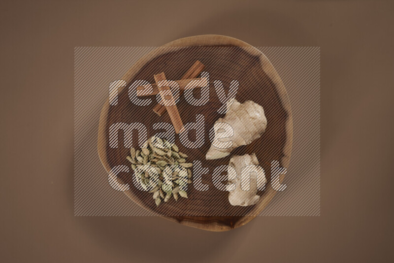 An assorted whole spices on a flat wooden tray including fresh and dried ginger, cinnamon sticks, cardamom, turmeric fingers, cloves, star anise on beige background