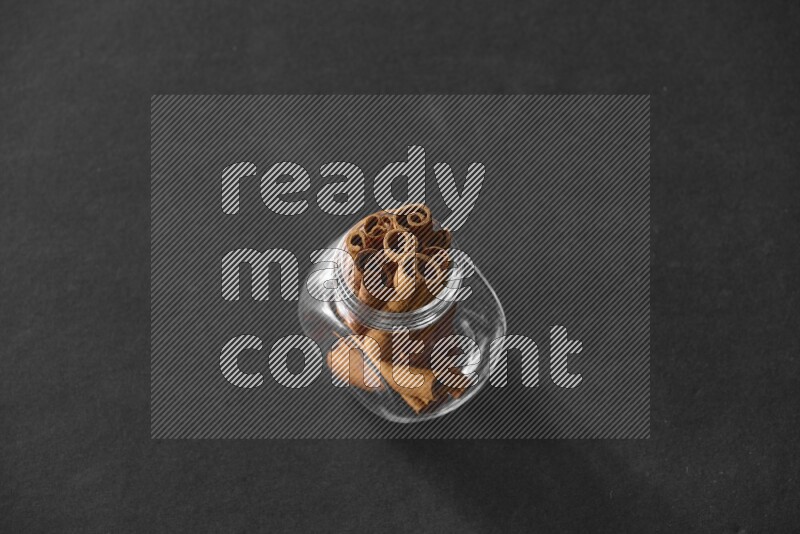 A glass spice jar full of cinnamon sticks on black flooring