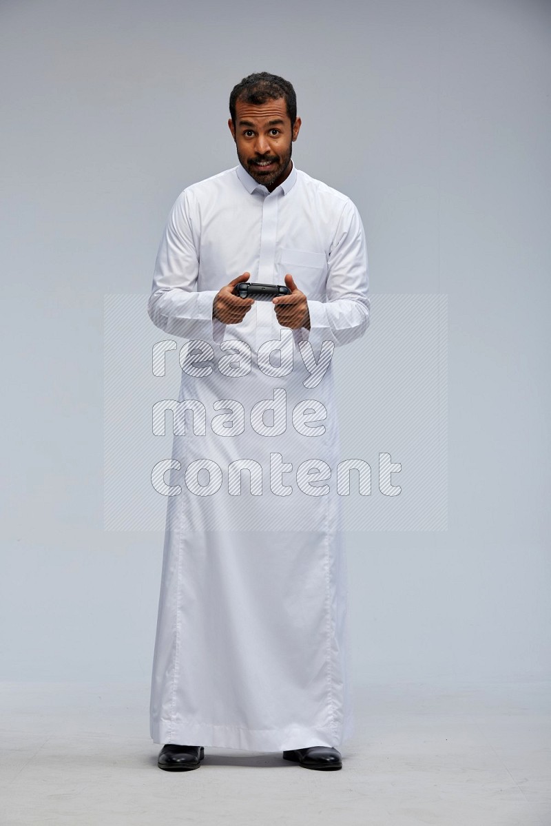 Saudi man Wearing thob standing holding joystick on Gray background