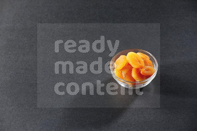 A glass bowl full of dried apricots on a black background in different angles
