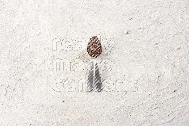 2 metal spoons full of flax on a textured white flooring in different angles