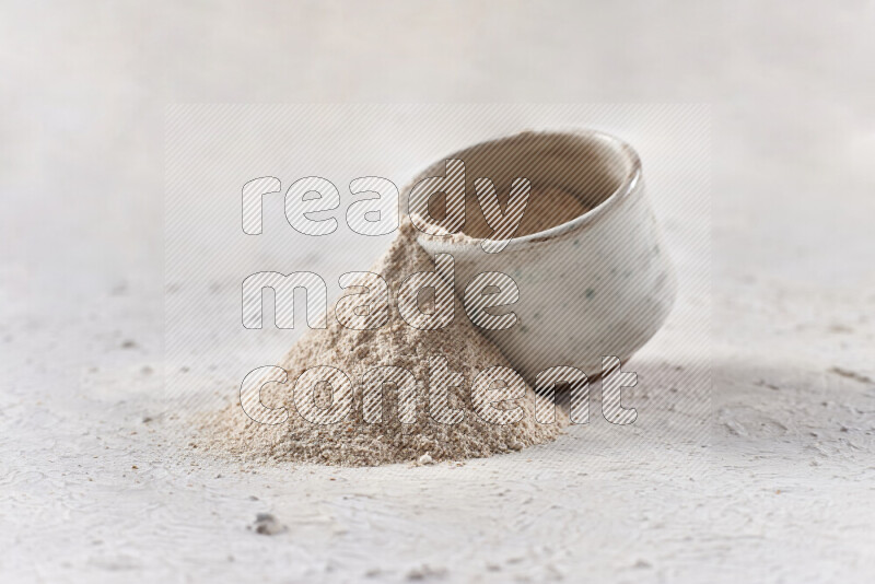 A beige pottery bowl full of onion powder with fallen powder from it on white background