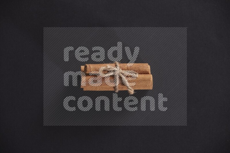 4 Cinnamon sticks stacked and bounded on black flooring