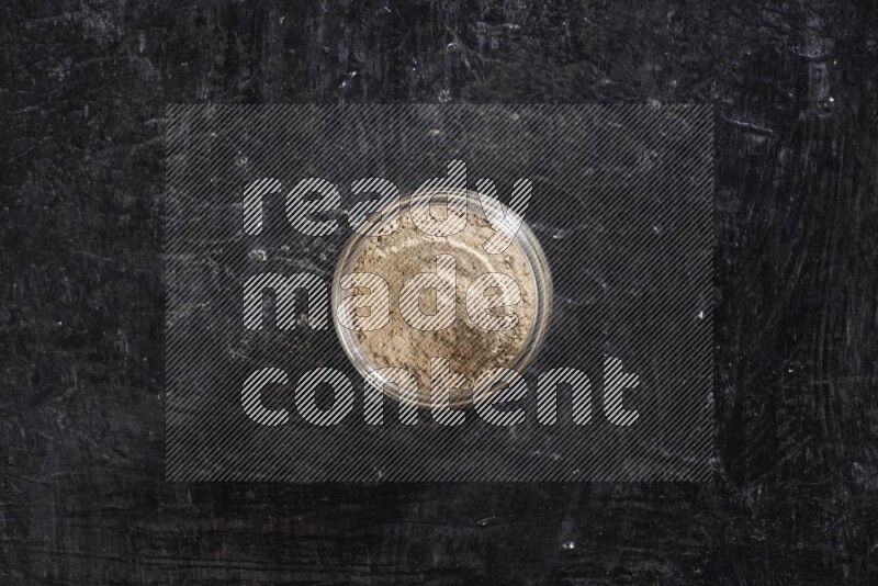 A glass jar full of garlic powder on a textured black flooring