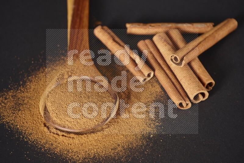 Cinnamon powder in a spoon ladle and spreaded on the floor beside it cinnamon sticks on the floor on black background in different angles