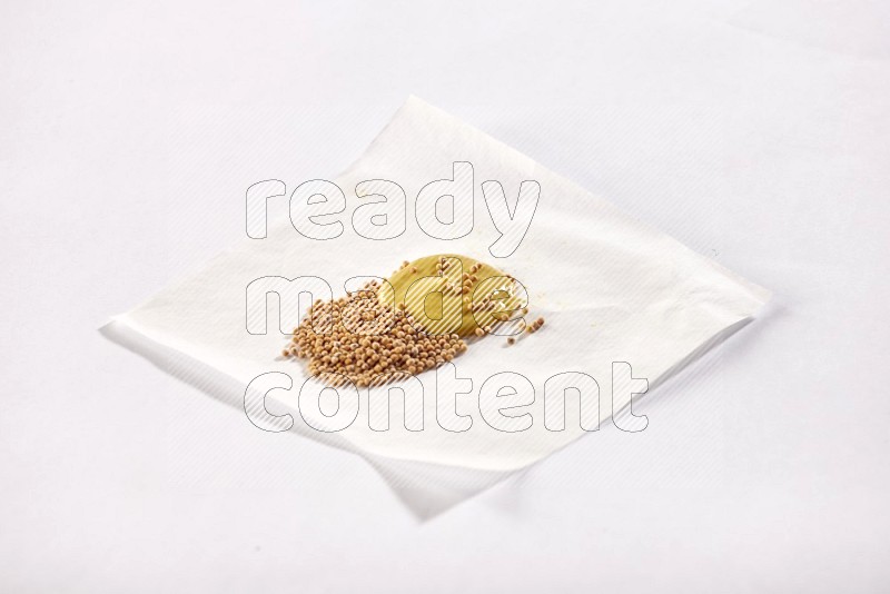 Mustard seeds and mustard paste on a piece of white paper on white flooring