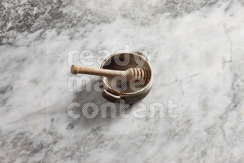 Multicolored Pottery bowl with wooden honey handle in it, on grey marble flooring, 65 degree angle