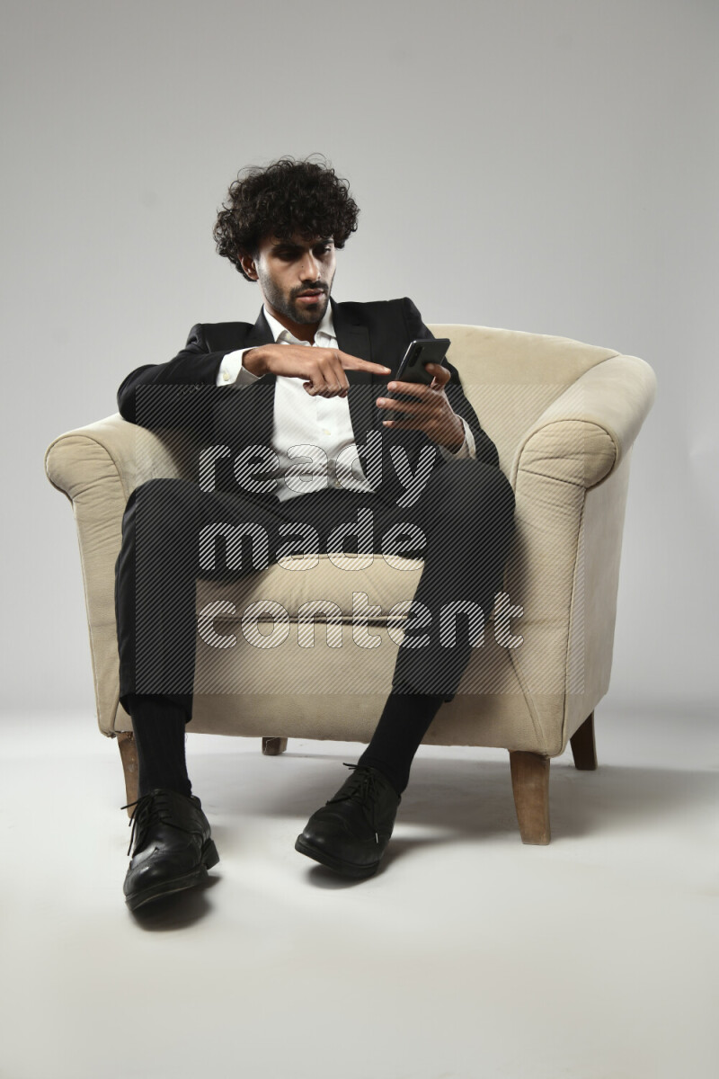 A man wearing formal sitting on a chair browsing on the phone on white background
