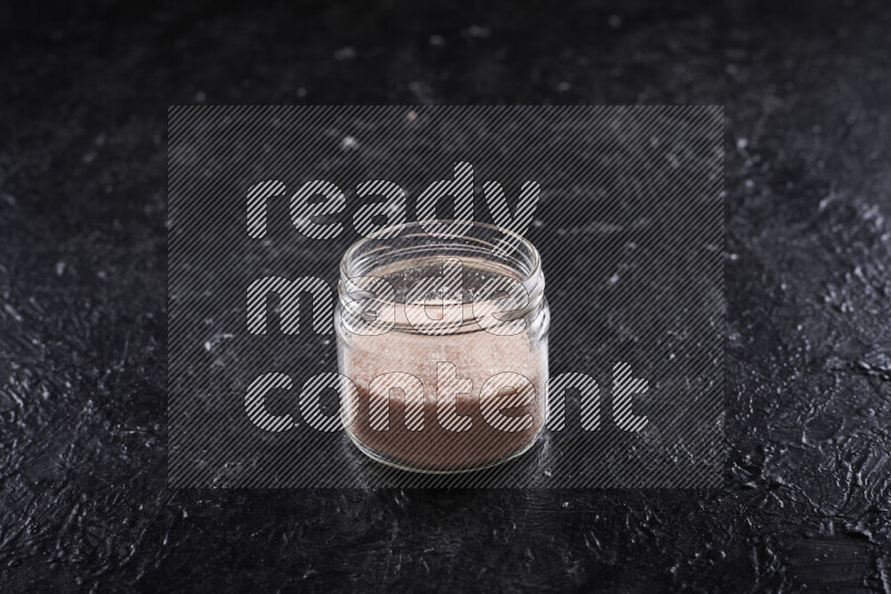 A glass jar full of fine himalayan salt on black background