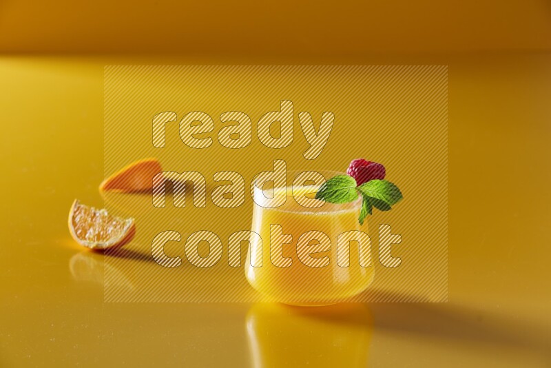 glass of orange juice with berry & mint on yellow background