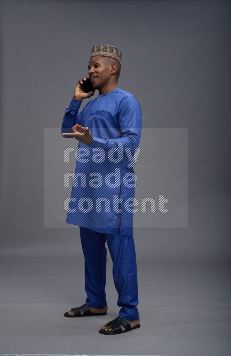 Man wearing Nigerian outfit standing talking on phone on gray background