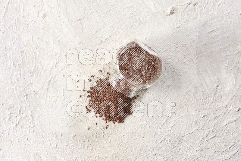 A glass spice jar full of flax flipped and flax spreaded out on a textured white flooring in different angles