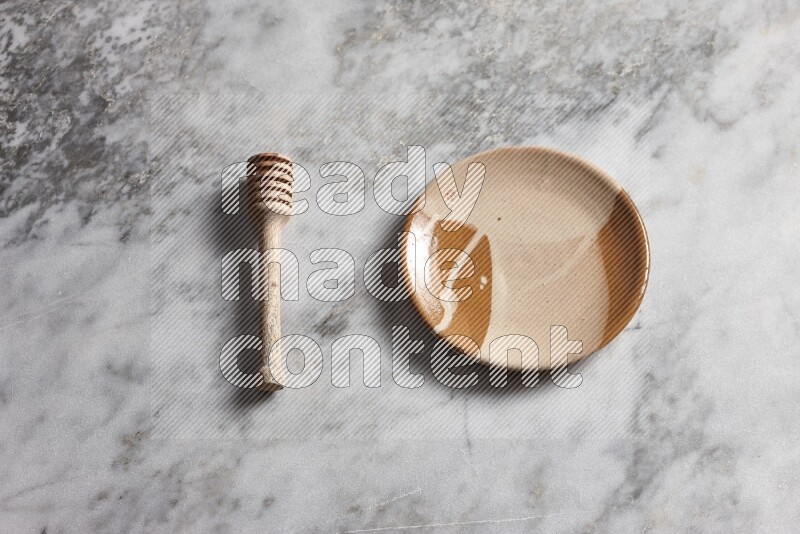 Multicolored pottery plate with wooden honey dipper on the side on grey marble background