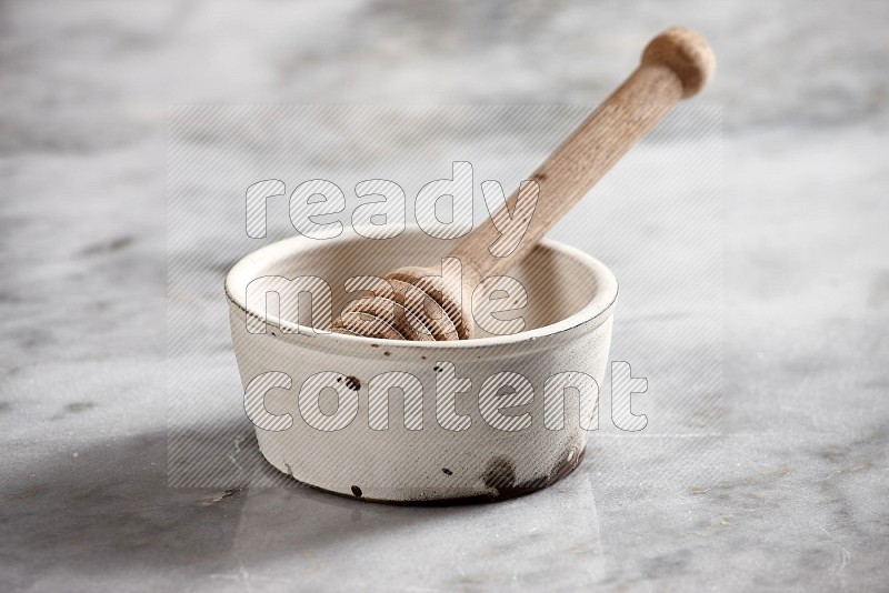 White Pottery bowl with wooden honey handle in it, on grey marble flooring, 15 degree angle