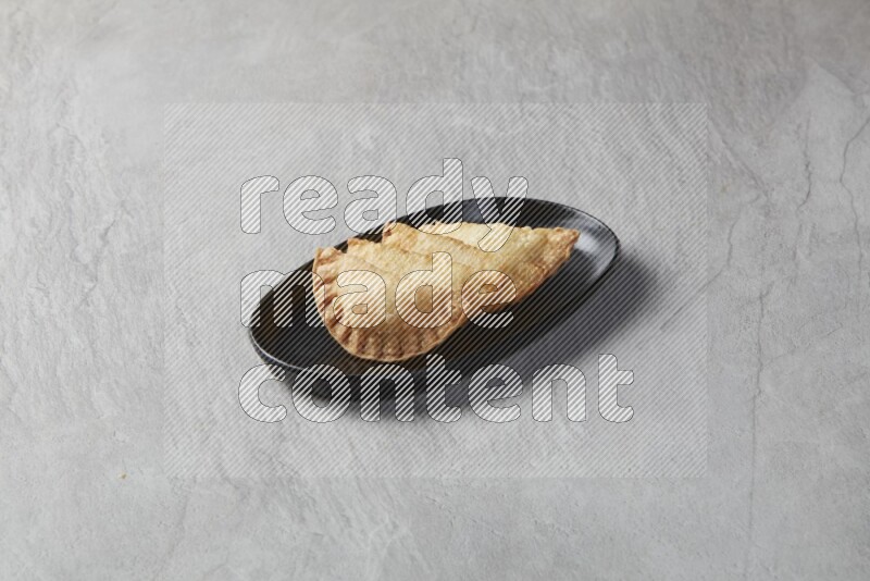 Four fried sambosas in an oval shaped black plate on a gray background