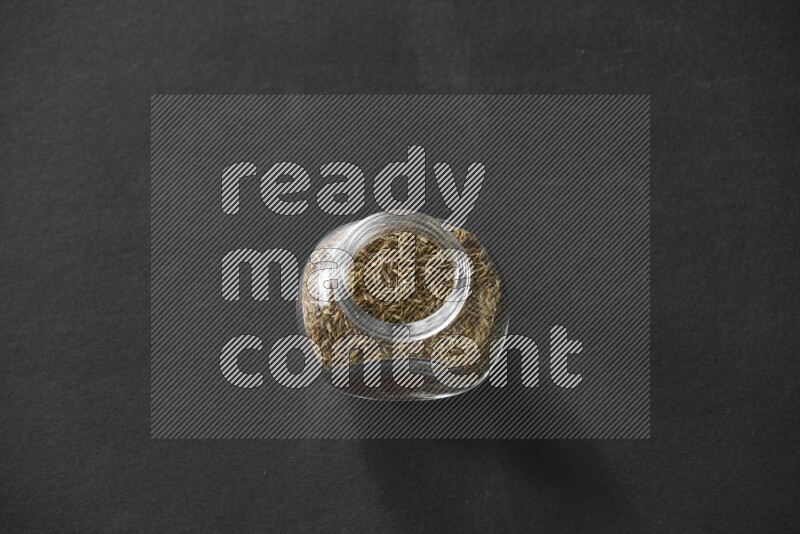 A glass spice jar full of cumin on black flooring