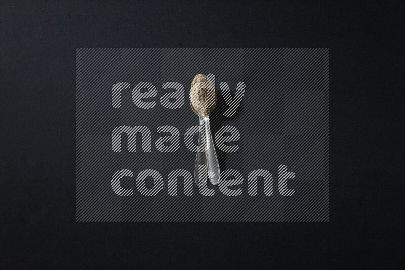 ملعقتان معدنيتان ممتلئتان ببودرة الهيل على خلفية سوداء