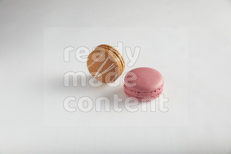 45º Shot of of two assorted Brown Irish Cream, and Pink Raspberry macarons on white background