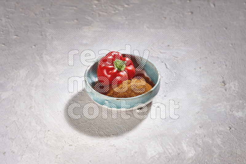 A colored pottery plate full of ground paprika powder and red bell pepper on white background