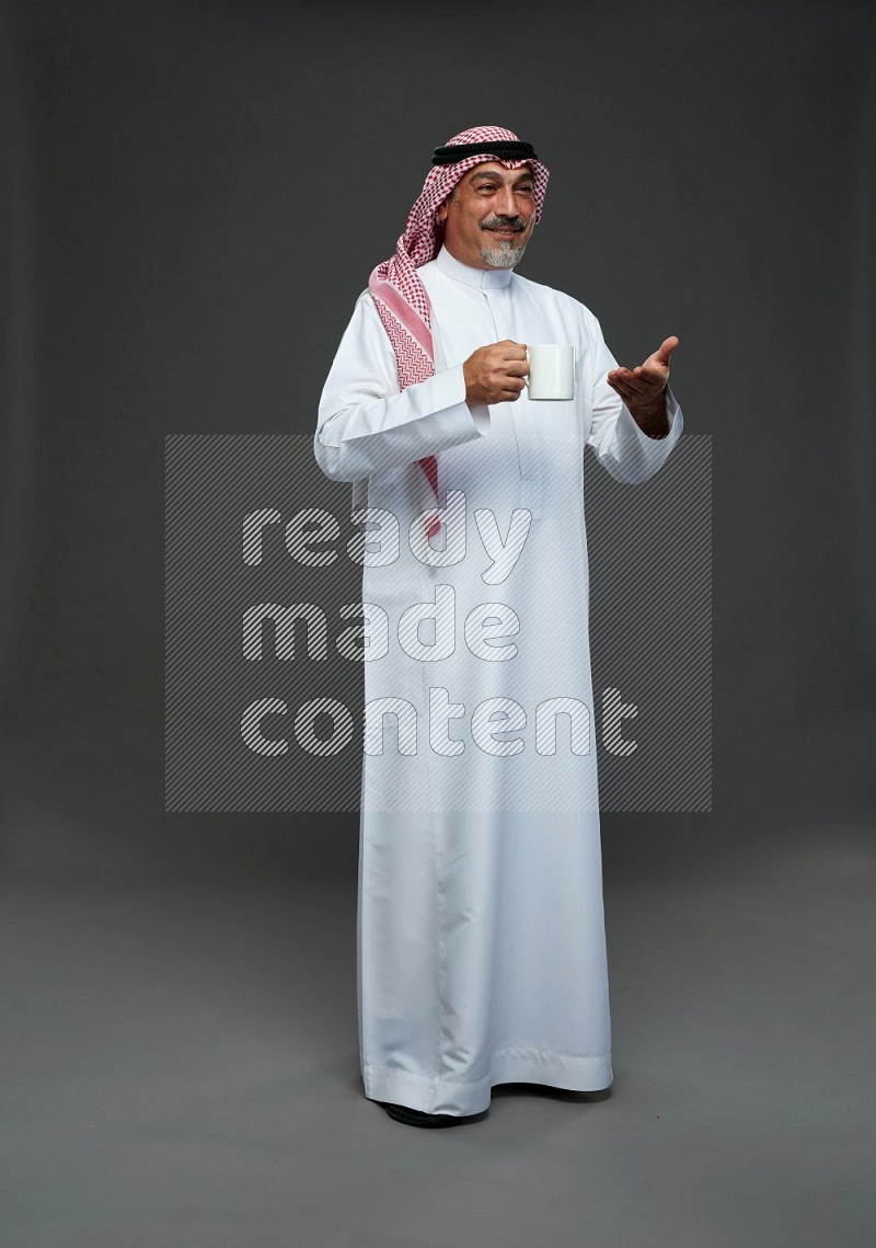 Saudi man with shomag Standing holding mug on gray background