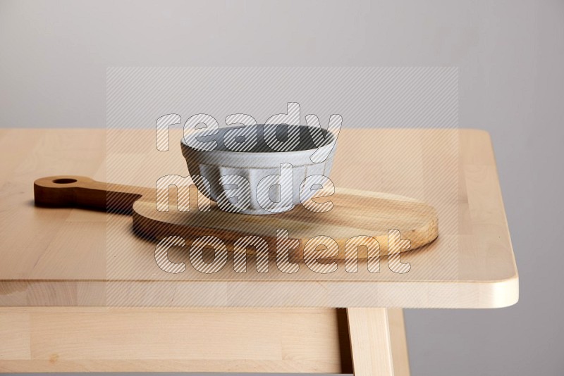 grey bowl placed on a  wooden oval cutting board on the edge of wooden table