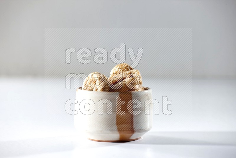 A beige ceramic bowl full of dried figs on a white background in different angles