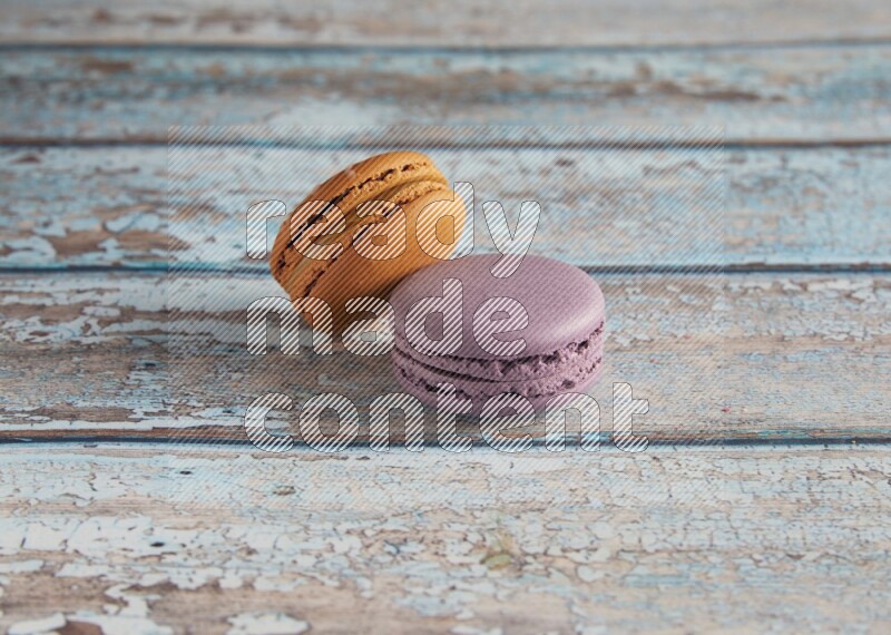 45º Shot of of two assorted Brown Irish Cream, and Purple Blueberry macarons  on light blue background