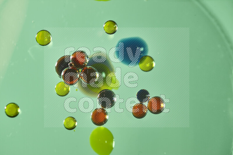 Close-ups of abstract red, blue and yellow watercolor drops on oil Surface on green background