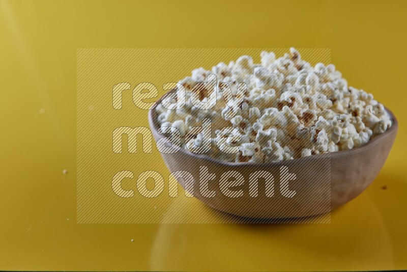 A brown pottery bowl full of popcorn on a yellow background in different angles