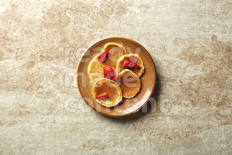 Five stacked strawberry mini pancakes in a brown plate on beige background