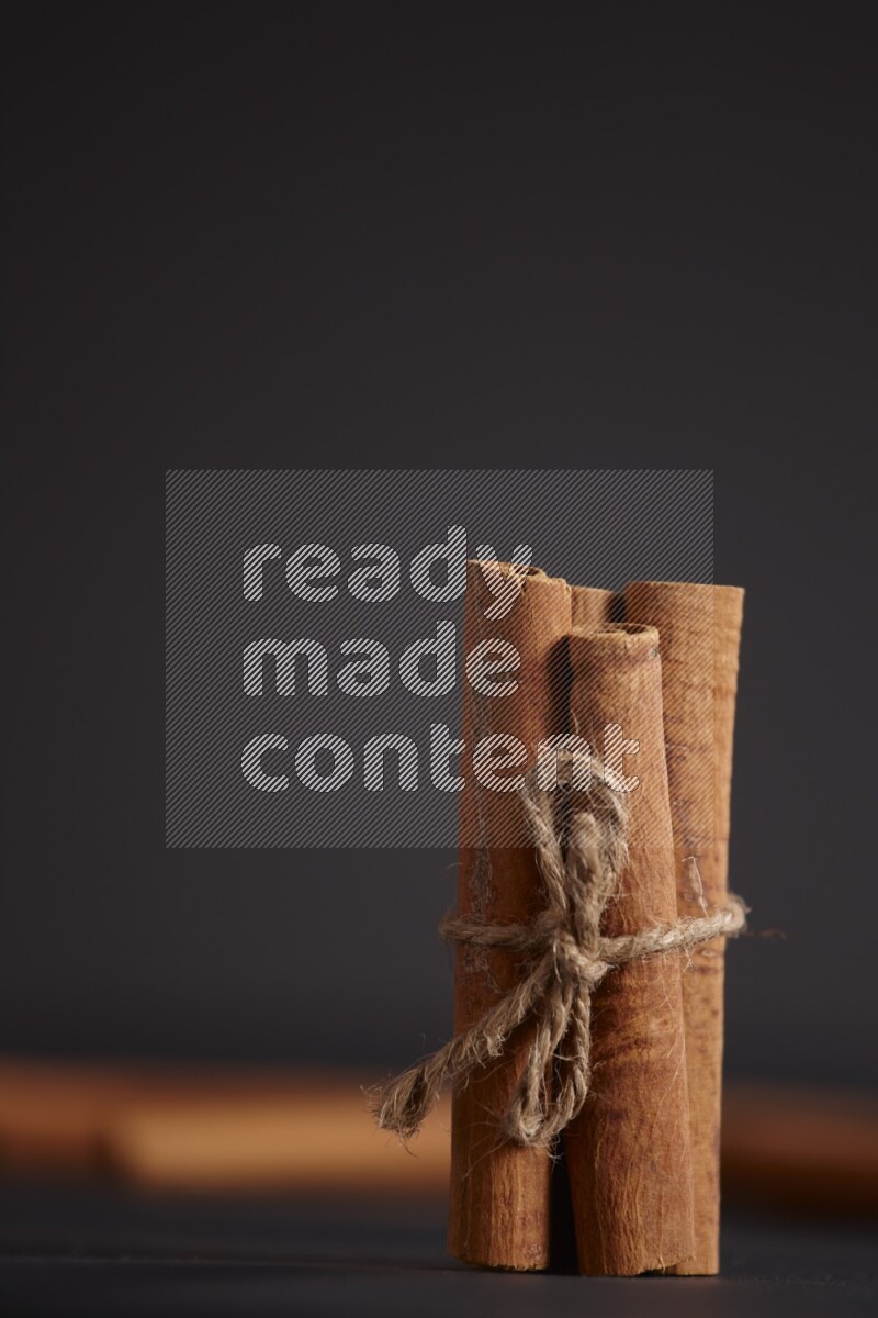 4 Cinnamon sticks stacked and bounded with more sticks in the background on black flooring