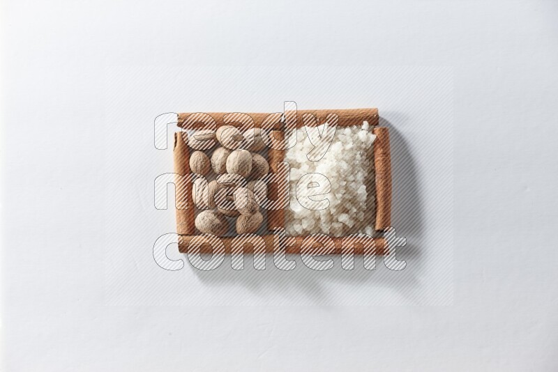 مربعان من أعواد القرفة ممتلئان بالملح الأبيض وجوزة الطيب علي خلفية بيضاء