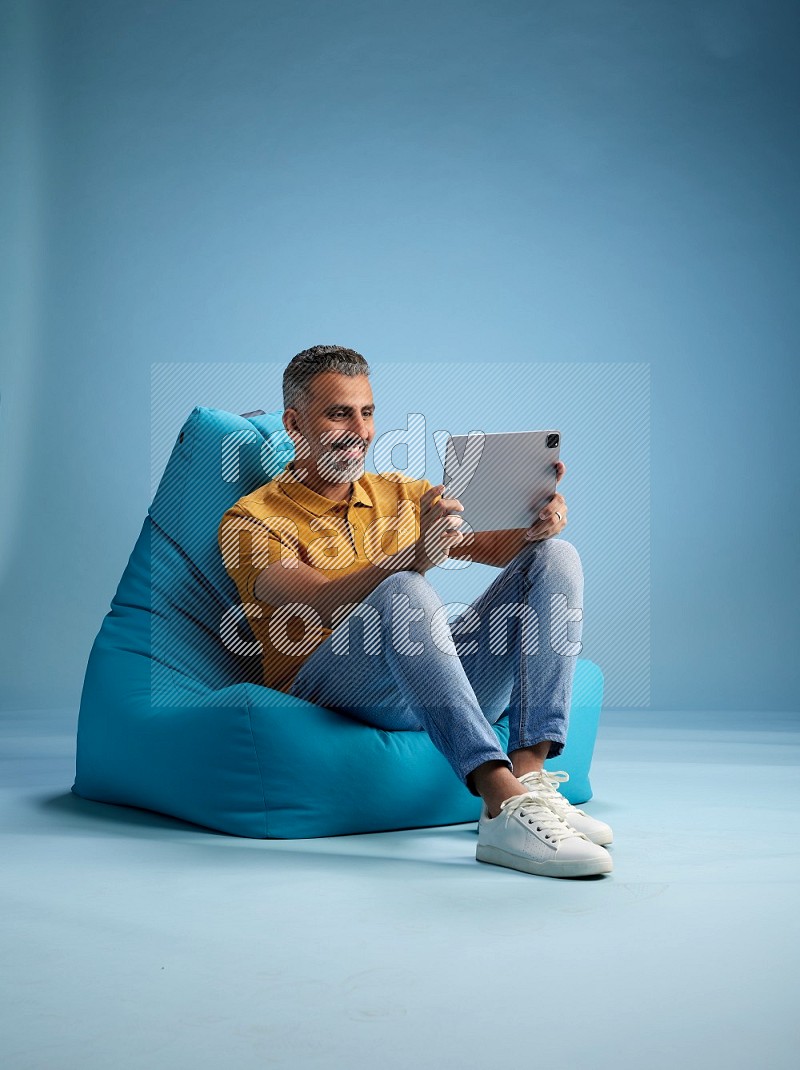 A man sitting on a blue beanbag and working on tablet