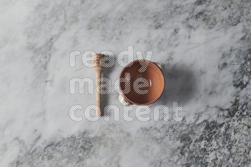 Brown pottery bowl with wooden honey dipper on the side on grey marble background