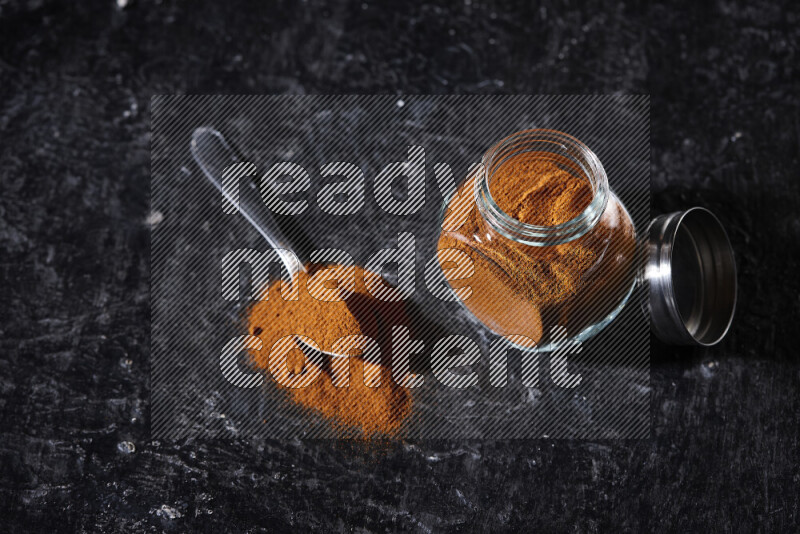 A glass jar full of ground paprika powder on black background