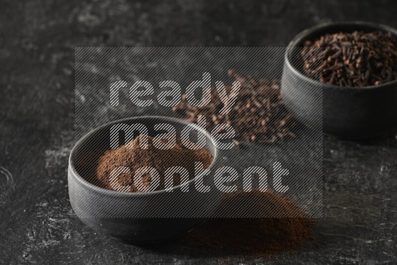 وعاءين من الفخار الأسود أحدهما ممتلئي بحبوب القرنفل والآخر ممتلئ ببودرة القرنفل على خلفية سوداء