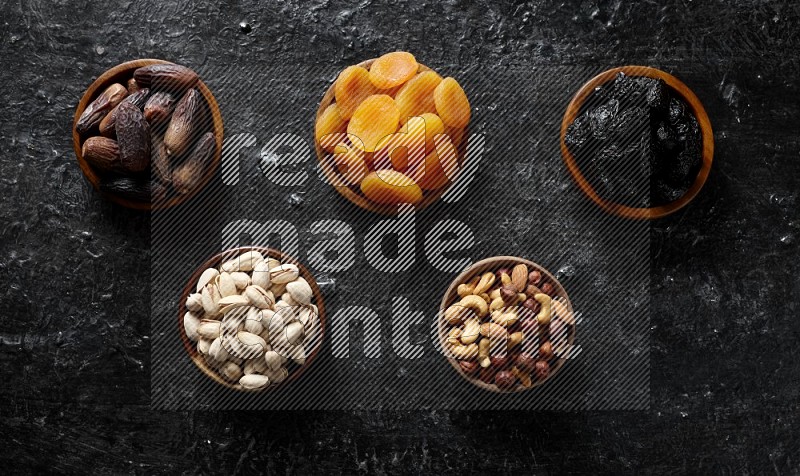 Dried fruits and nuts in wooden bowls in a dark setup