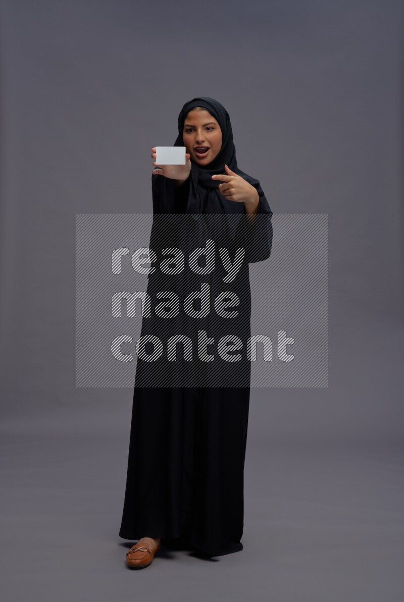 Saudi woman wearing Abaya standing holding ATM card on gray background
