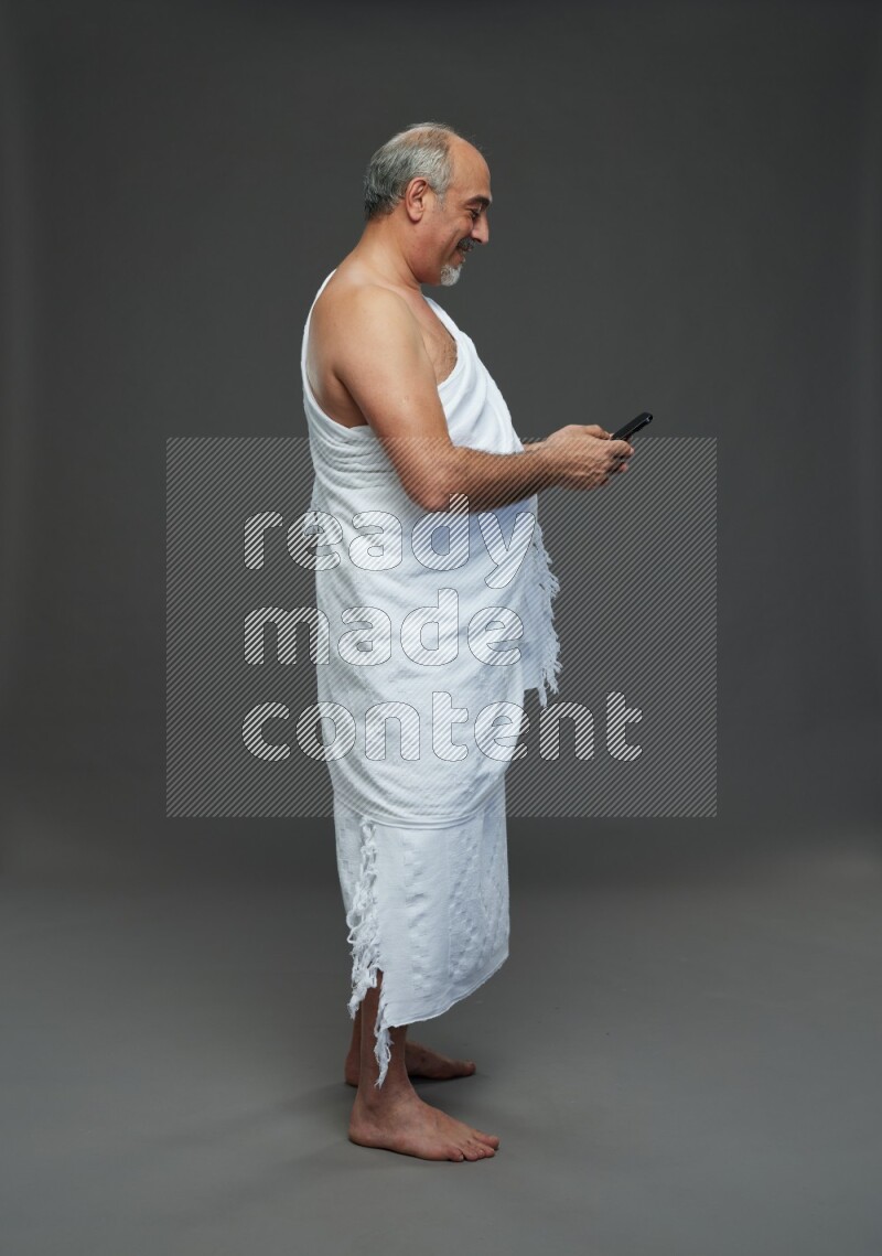 A man wearing Ehram Standing texting on phone on gray background