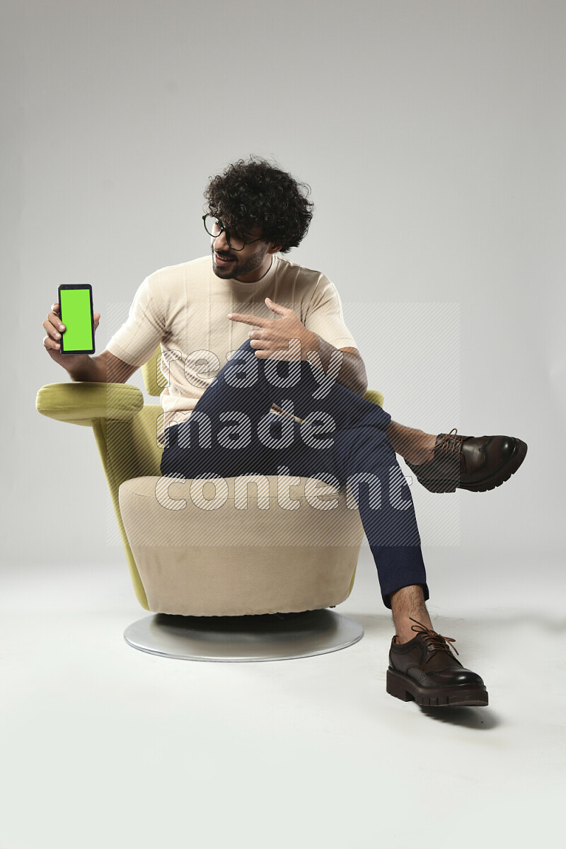 A man wearing casual sitting on a chair showing a phone screen on white background