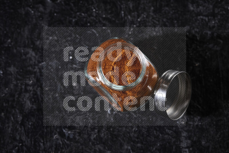 A glass jar full of ground paprika powder on black background